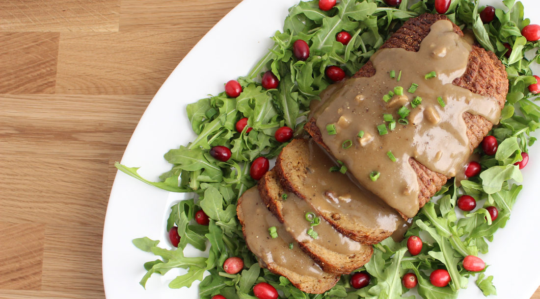 Overhead view of a Field Roast loaf on a bed of arugula and cranberries on white plate