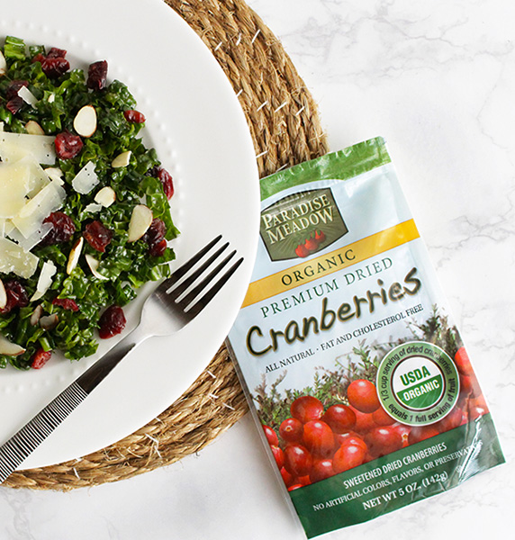 kale salad on white plate with cranberries, cheese, and a page of paradise meadow organic cranberries