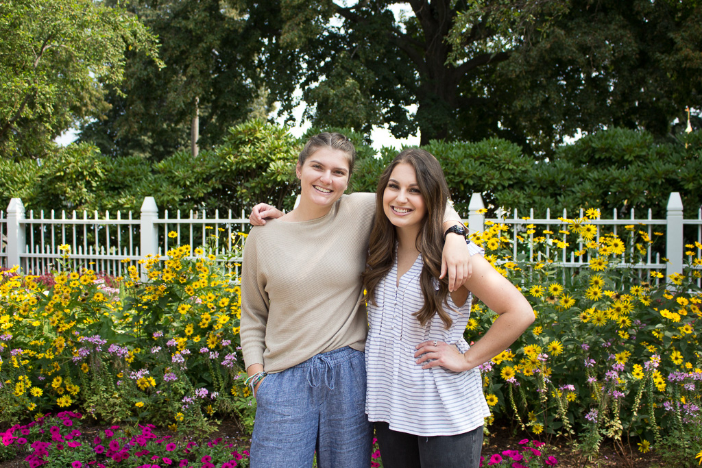 two women posing in front of a garden